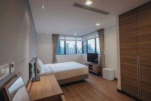 A hotel room with a bed, a TV, a desk, and a view of the cityscape. - Novotel Living Singapore Orchard (Singapore)