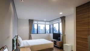 Habitación de hotel moderna con una cama, un escritorio, un televisor y vistas a la ciudad.