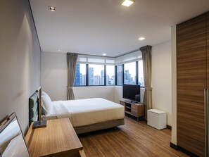 A modern hotel room with a bed, a desk, a TV, and a view of the cityscape.