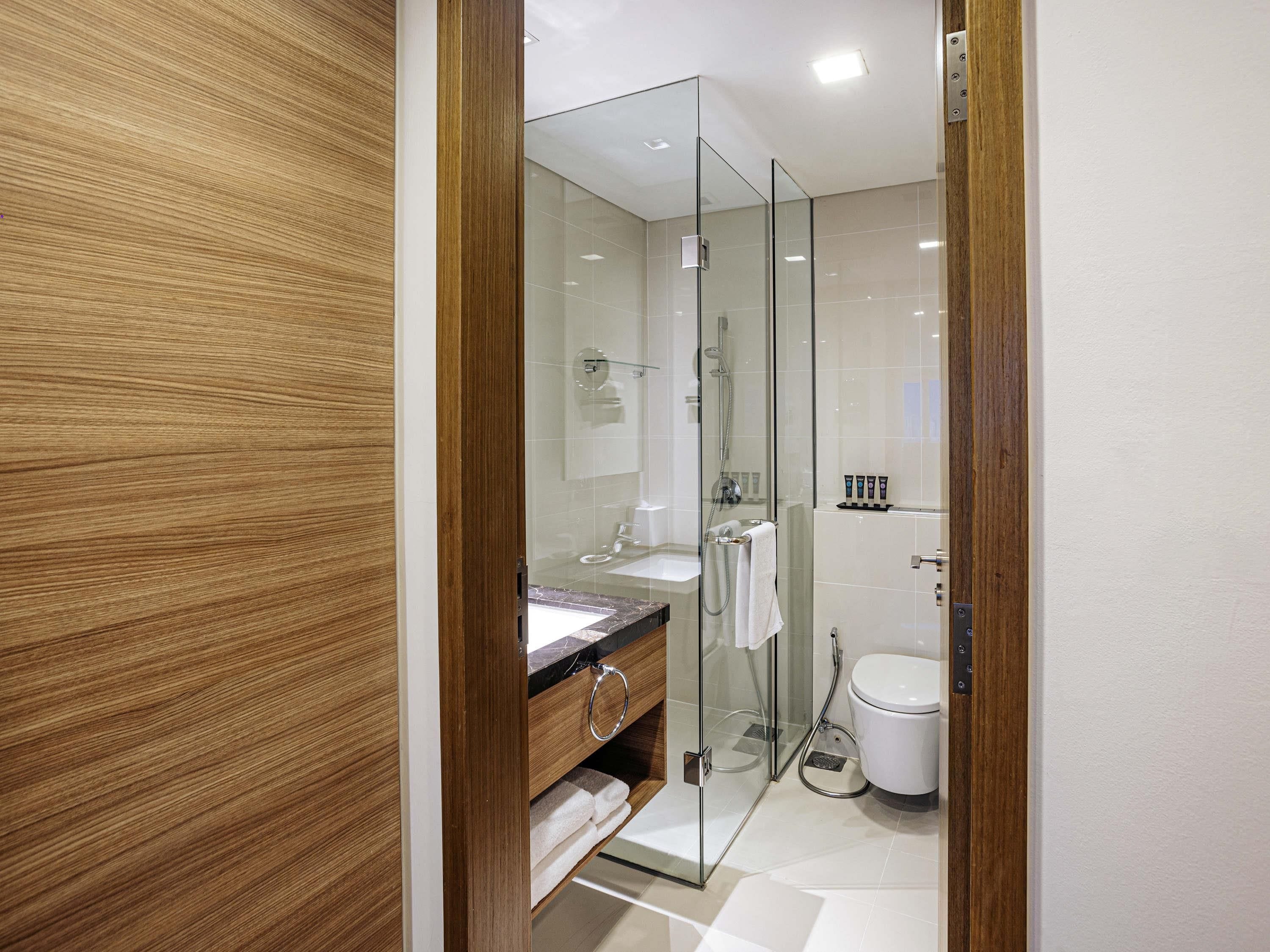 Une salle de bain moderne avec une douche à parois de verre, un meuble-lavabo en bois et des toilettes blanches.