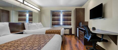 Habitación de hotel con dos camas, un escritorio, una silla, un televisor y una ventana con cortinas.