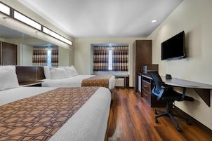 Habitación de hotel con dos camas, un escritorio, una silla, un televisor y una ventana con cortinas.