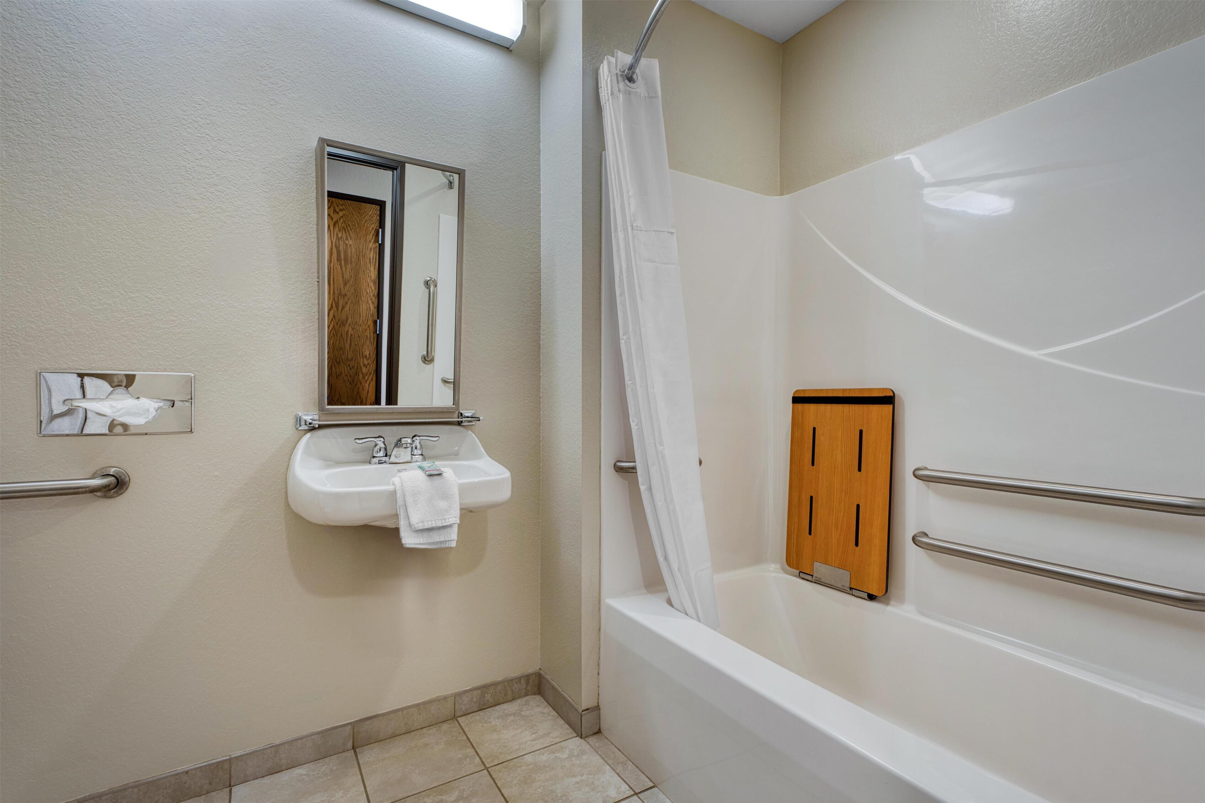 A bathroom with a sink, mirror, shower, and wooden panel.