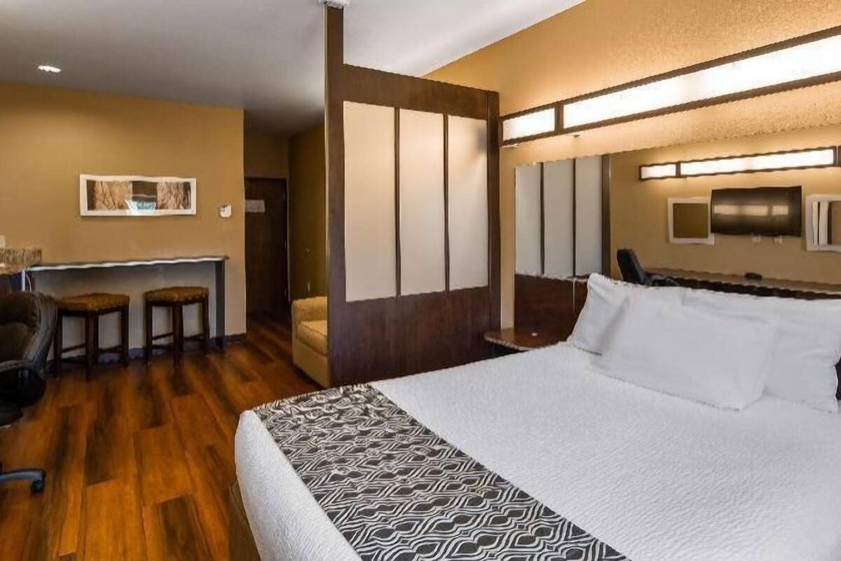 Habitación de hotel con cama, escritorio con dos sillas, televisor y lámpara fijada a la pared.