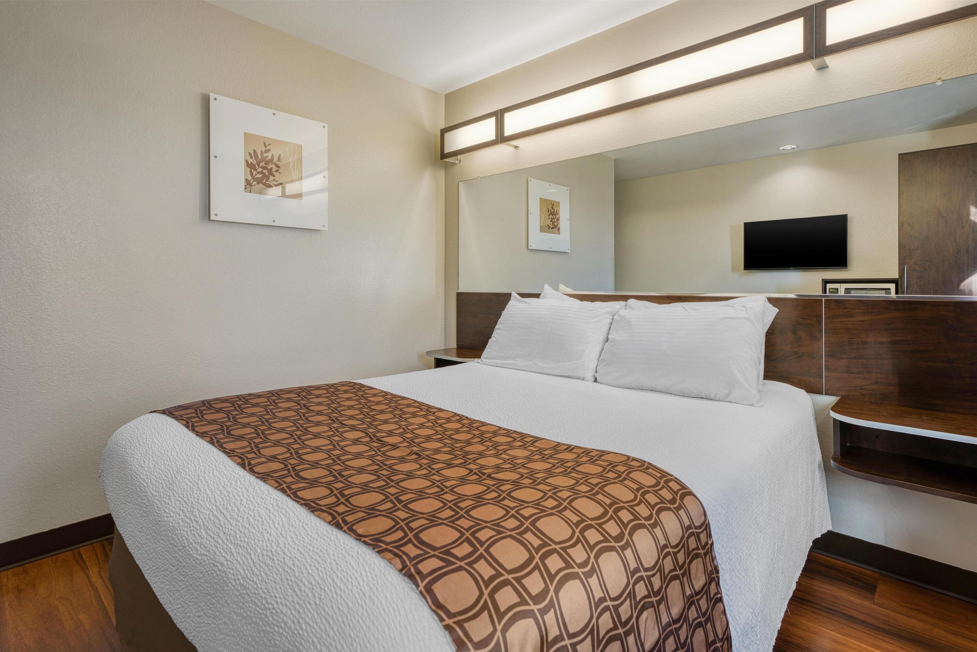 A hotel room with a large bed, a flat-screen TV, and a wooden headboard.