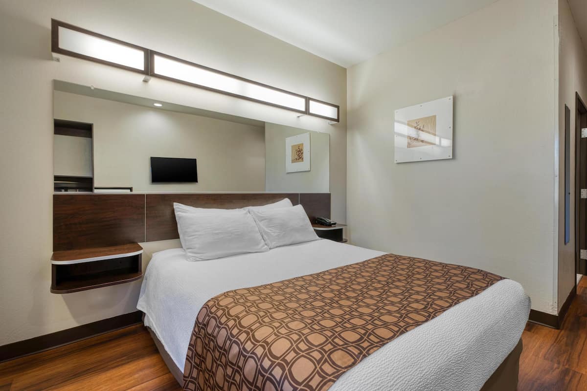 Habitación de hotel con una cama grande, un televisor de pantalla plana montado en la pared, una mesita de noche y un estante en la pared.