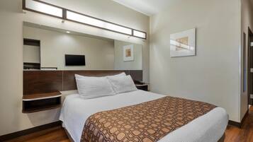 Habitación de hotel con una cama grande, un televisor de pantalla plana montado en la pared, una mesita de noche y un estante en la pared.