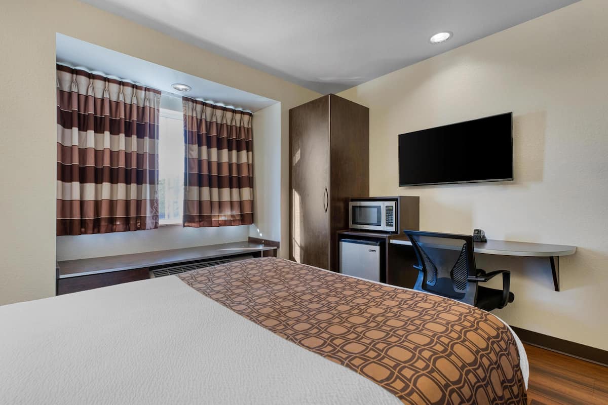 Una habitación de hotel con una cama, un escritorio con computadora, un televisor y un refrigerador pequeño.