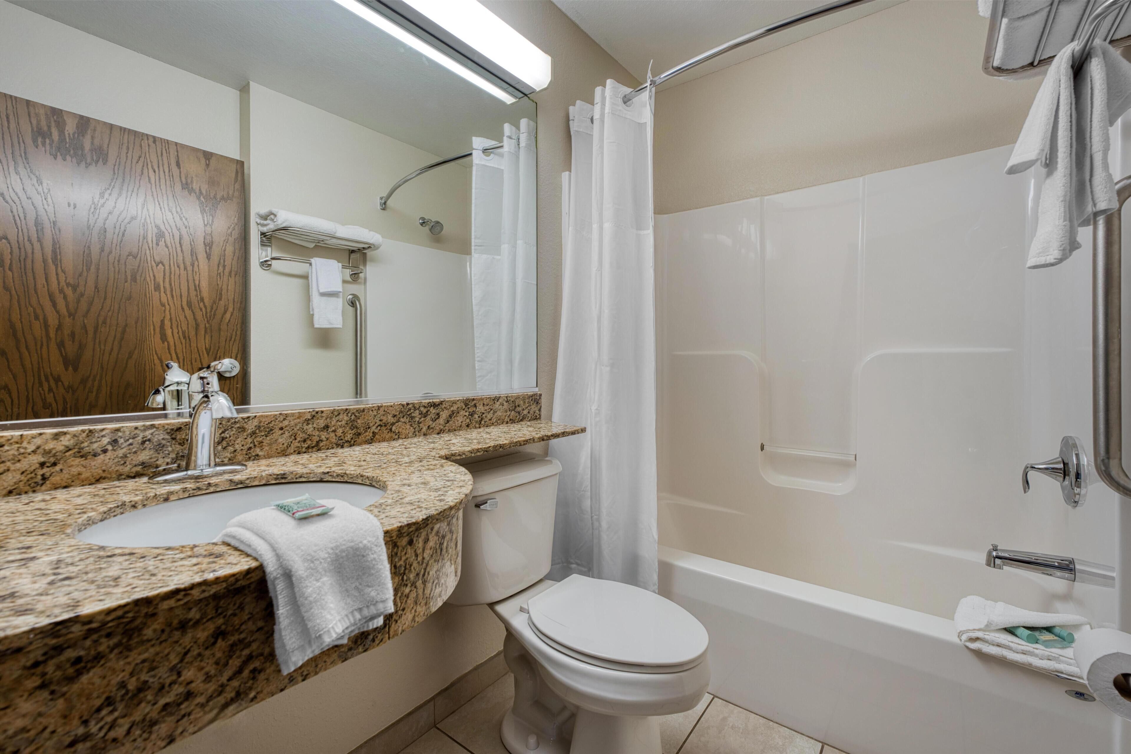 A bathroom with a granite countertop sink, a toilet, a bathtub, and a shower curtain.