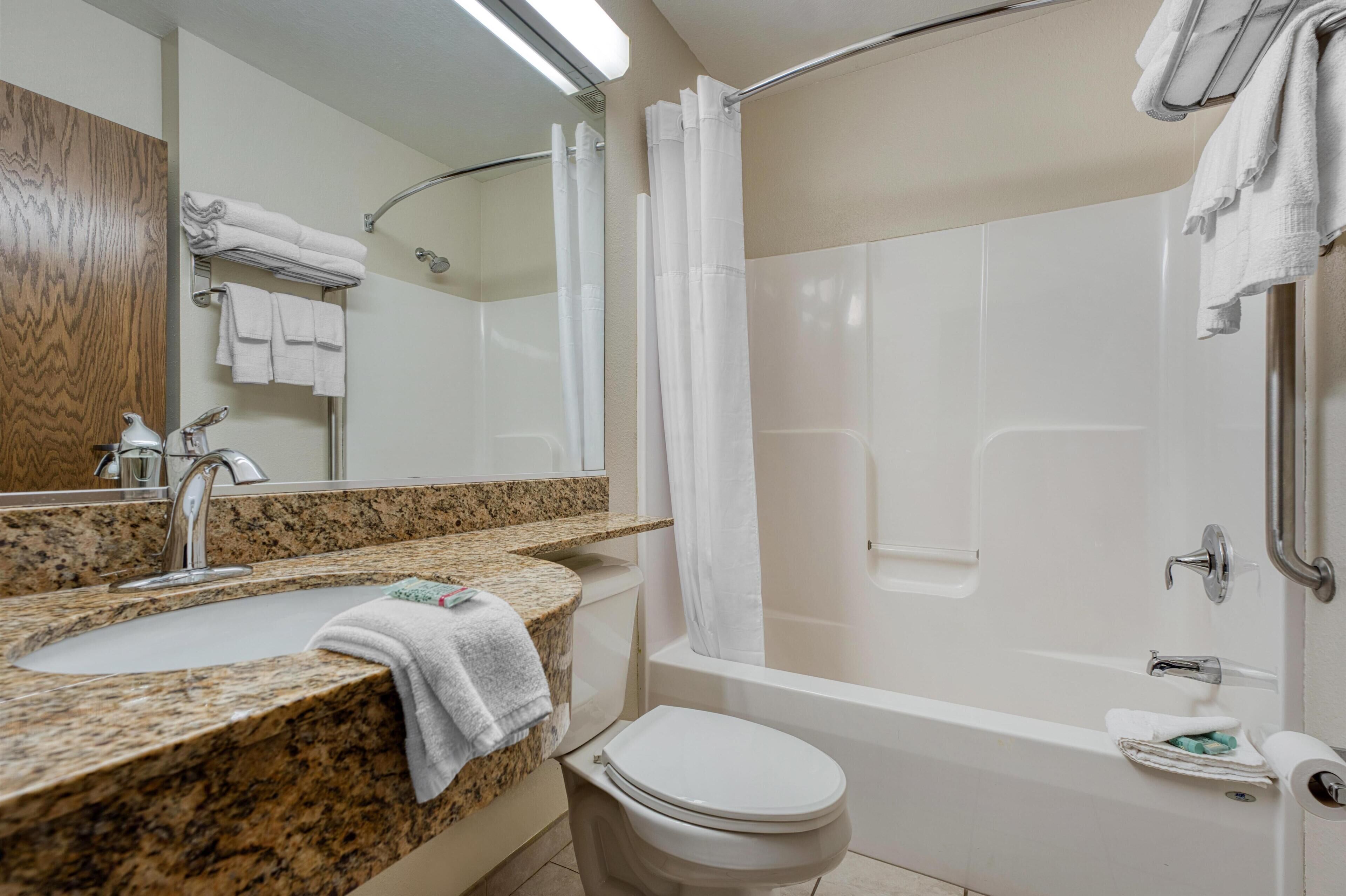 A bathroom with a granite countertop sink, a white toilet, a bathtub, and a shower curtain.