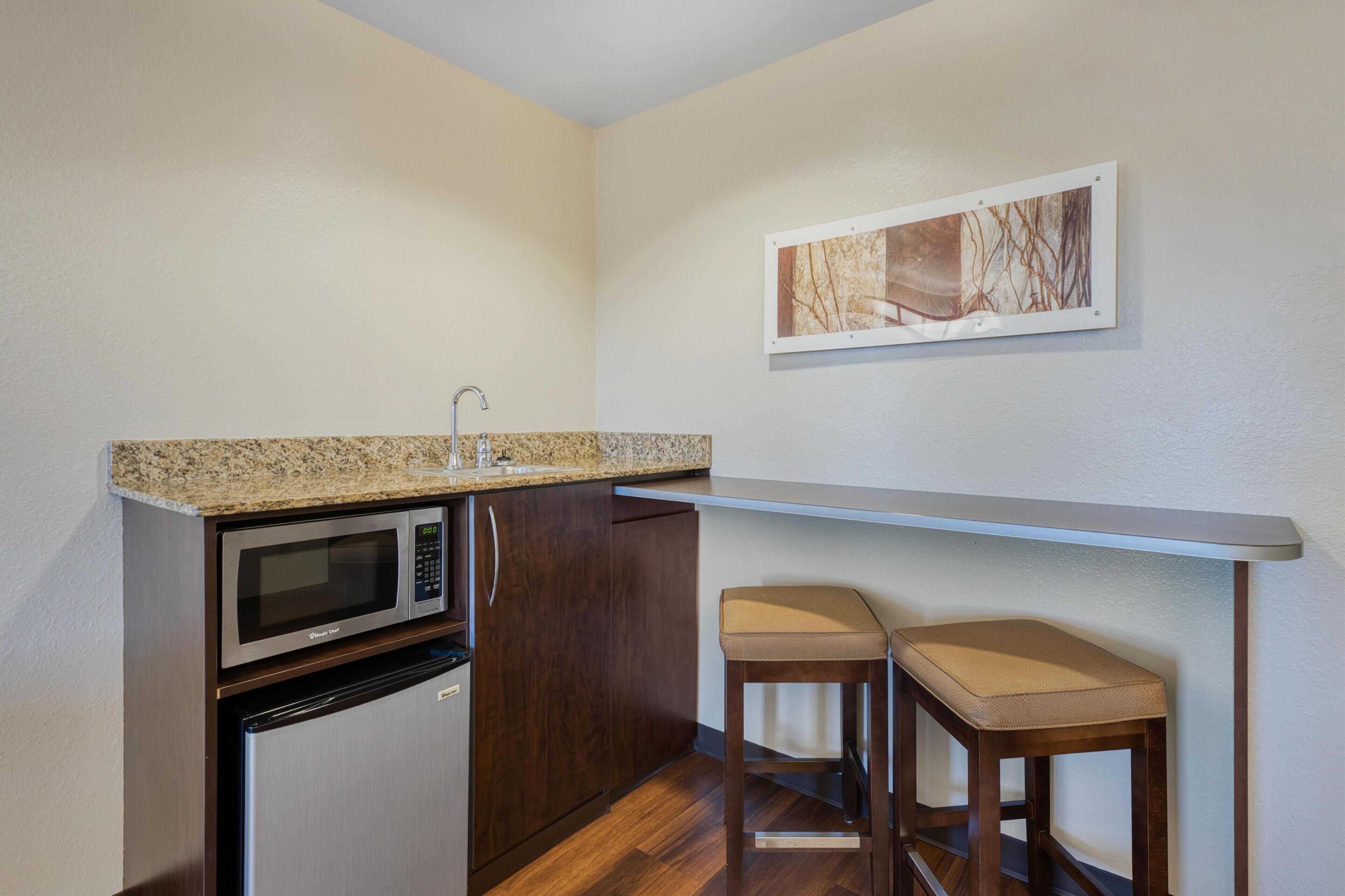 Una cocina compacta con microondas, refrigerador y un taburete pequeño.