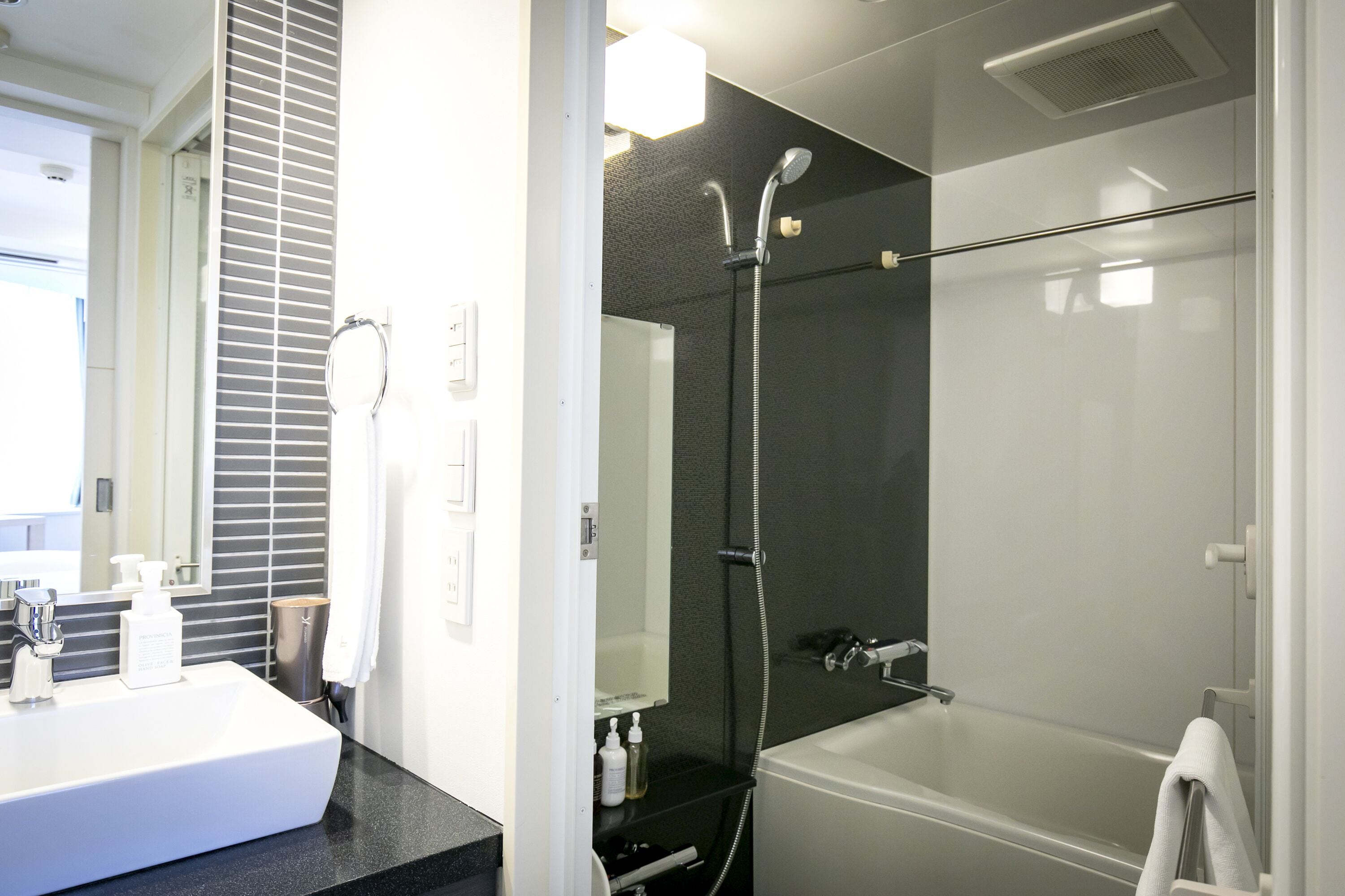 Un baño moderno con un lavamanos grande de color blanco, un espejo, una ducha con cabezal de ducha de mano y una bañera.