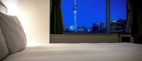 A hotel room with a bed and a window offering a nighttime view of a tall tower.