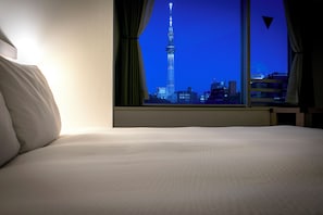 Habitación de hotel con cama y ventana que ofrece vista nocturna de una torre alta.