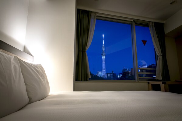 Ein Hotelzimmer mit Bett, Fenster mit Vorhängen und Blick auf einen Turm bei Nacht.