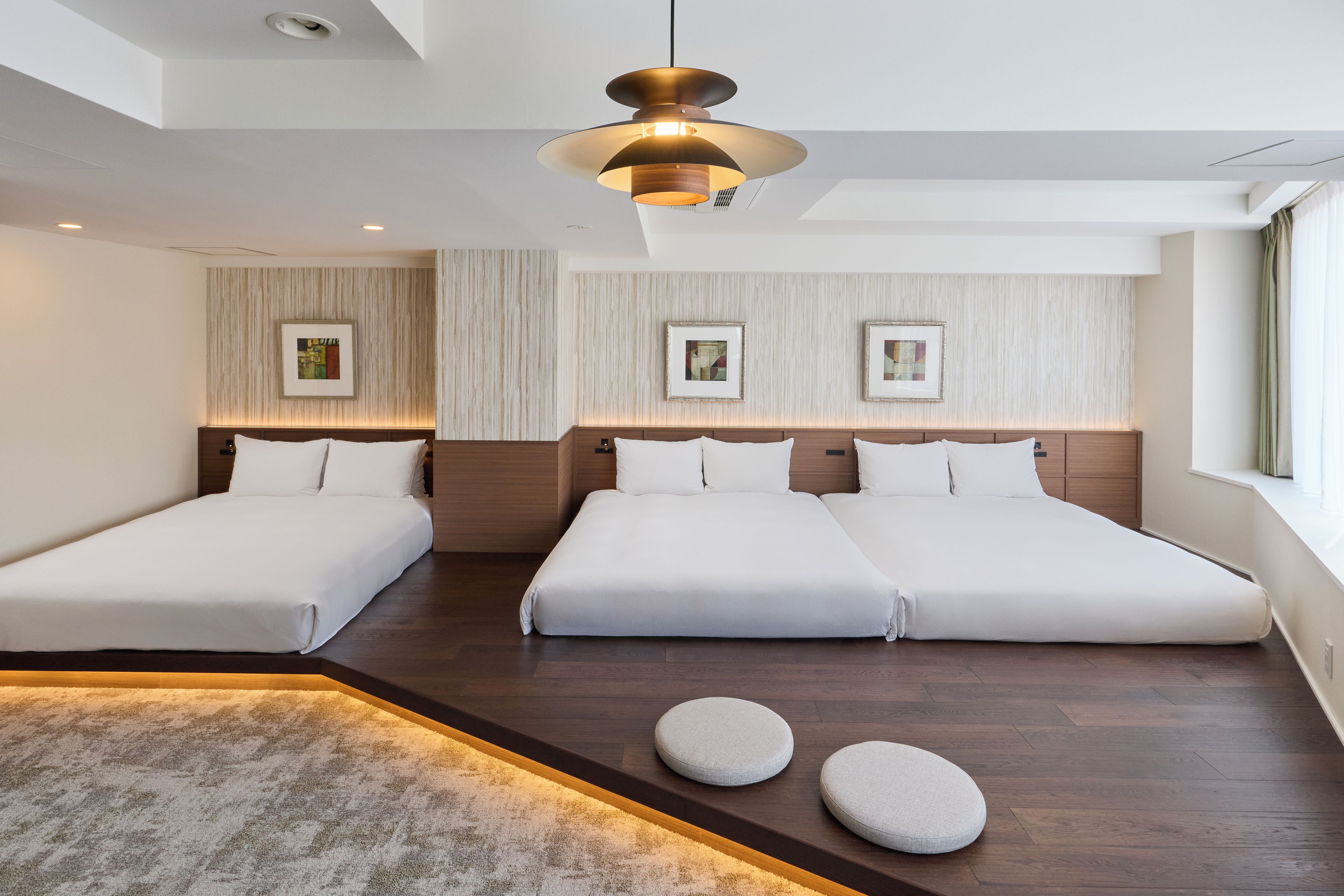 A hotel room with two single beds, a large window, and a modern ceiling light.