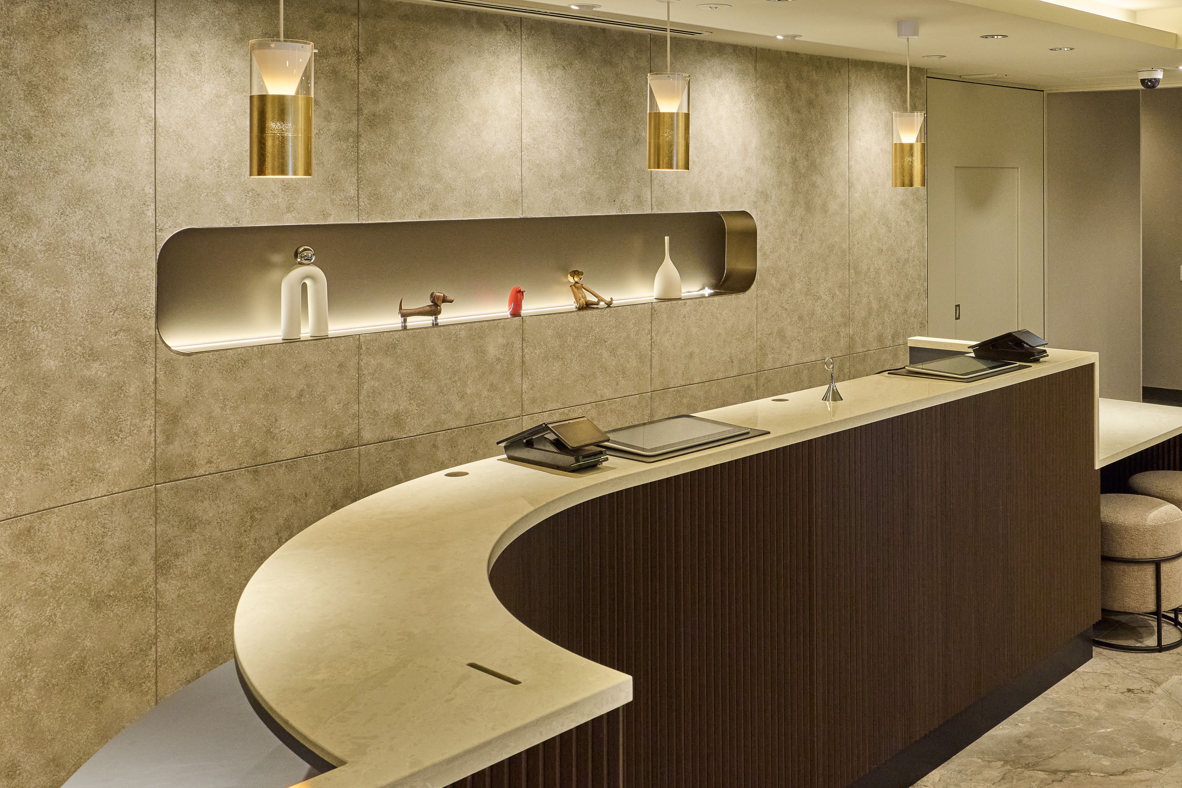 A reception desk with a curved design, a mirror above it, and a shelf with decorative items.
