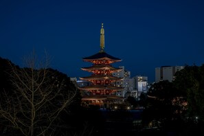 A multi-tiered pagoda with illuminated tiers and a golden spire, surrounded by trees and modern buildings. - Residential Hotel B:CONTE Asakusa (Tokyo)