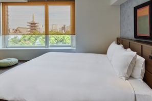 A hotel room with a large bed, a window with a view of traditional architecture, and a modern wall art piece.
