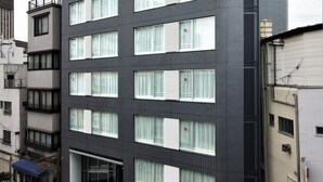 A multi-story hotel with a modern facade, large windows with blinds, and a red awning with signage. - Residential Hotel B:CONTE Asakusa (Tokyo)