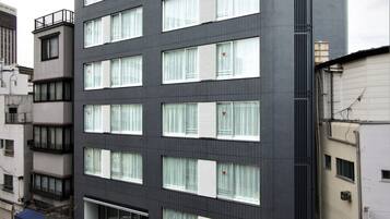Et hotel med flere etager, moderne facade, store vinduer med persienner og en rød markise med skilte.