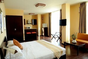 A hotel room with a bed, a sofa, a TV, a desk, and a small table with a vase.