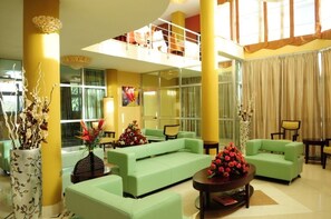 A spacious lobby with a high ceiling, green sofas, and decorative vases.