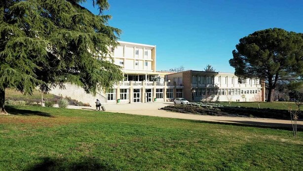 A two-story building with a central entrance, surrounded by a grassy area and trees. - Complexe Hôtelier Regain (Sainte-Tulle)