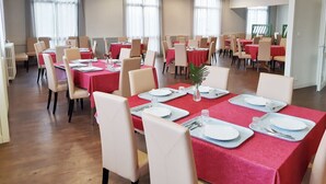 A dining area with multiple tables set for meals, featuring red tablecloths and white chairs. - Complexe Hôtelier Regain (Sainte-Tulle)