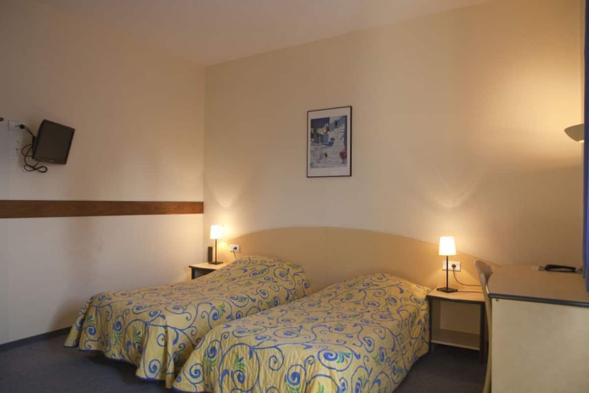 A hotel room with two single beds, a desk, a chair, a wall-mounted TV, and a framed picture on the wall.