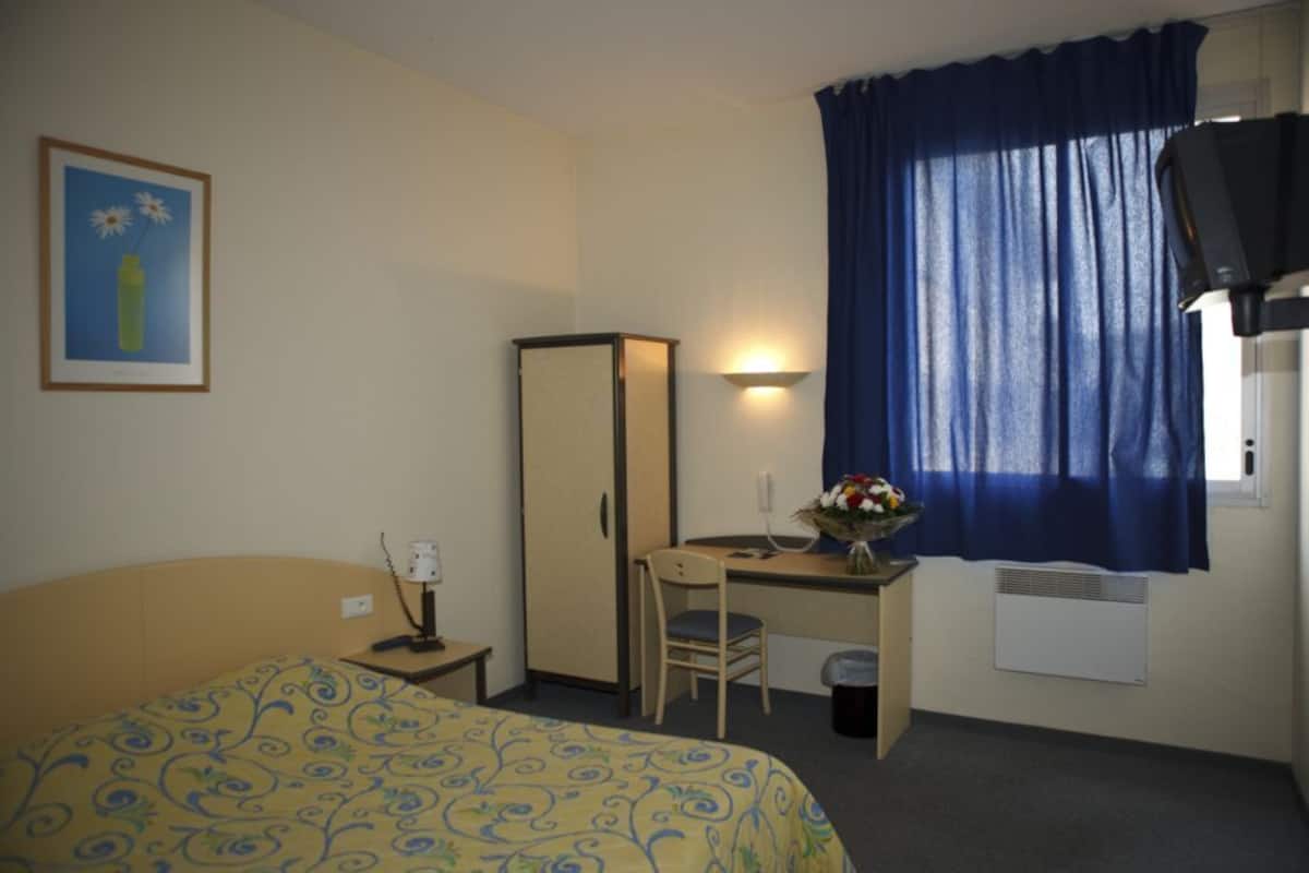 A hotel room with a bed, desk, chair, TV, and a window with curtains.