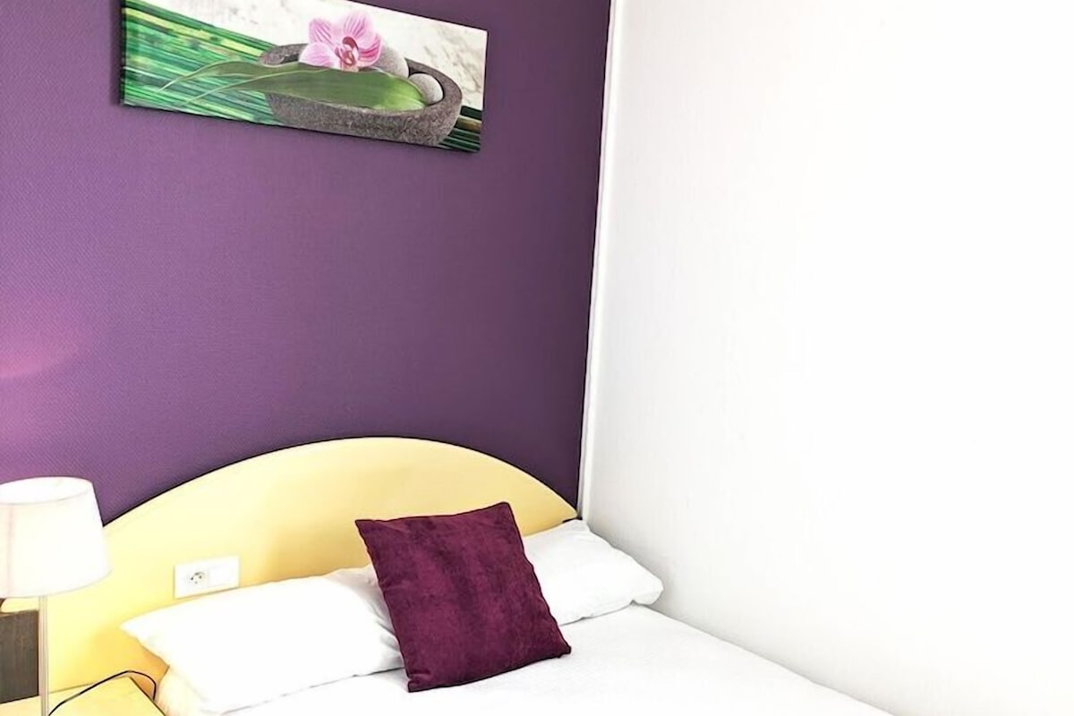 A hotel room with a bed, a nightstand, a lamp, and a painting on the wall.