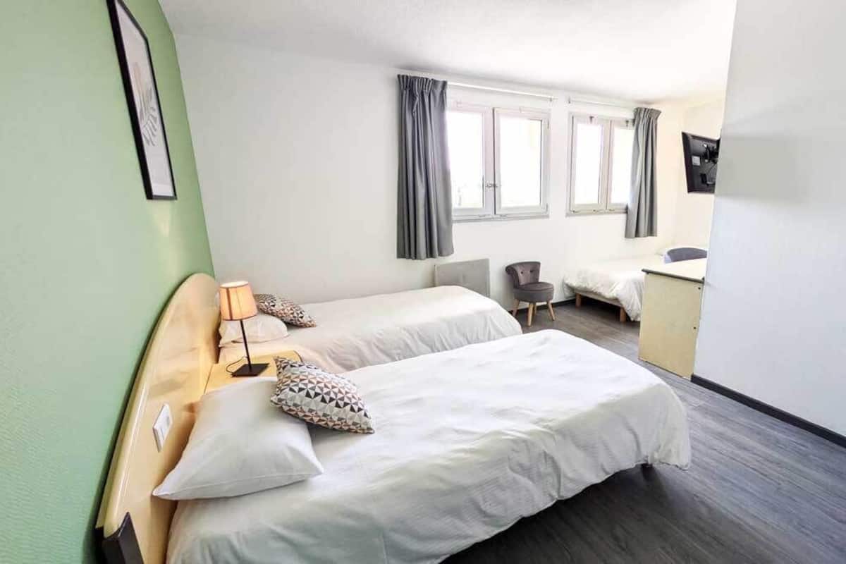 A hotel room with two beds, a desk, a chair, and a wardrobe.