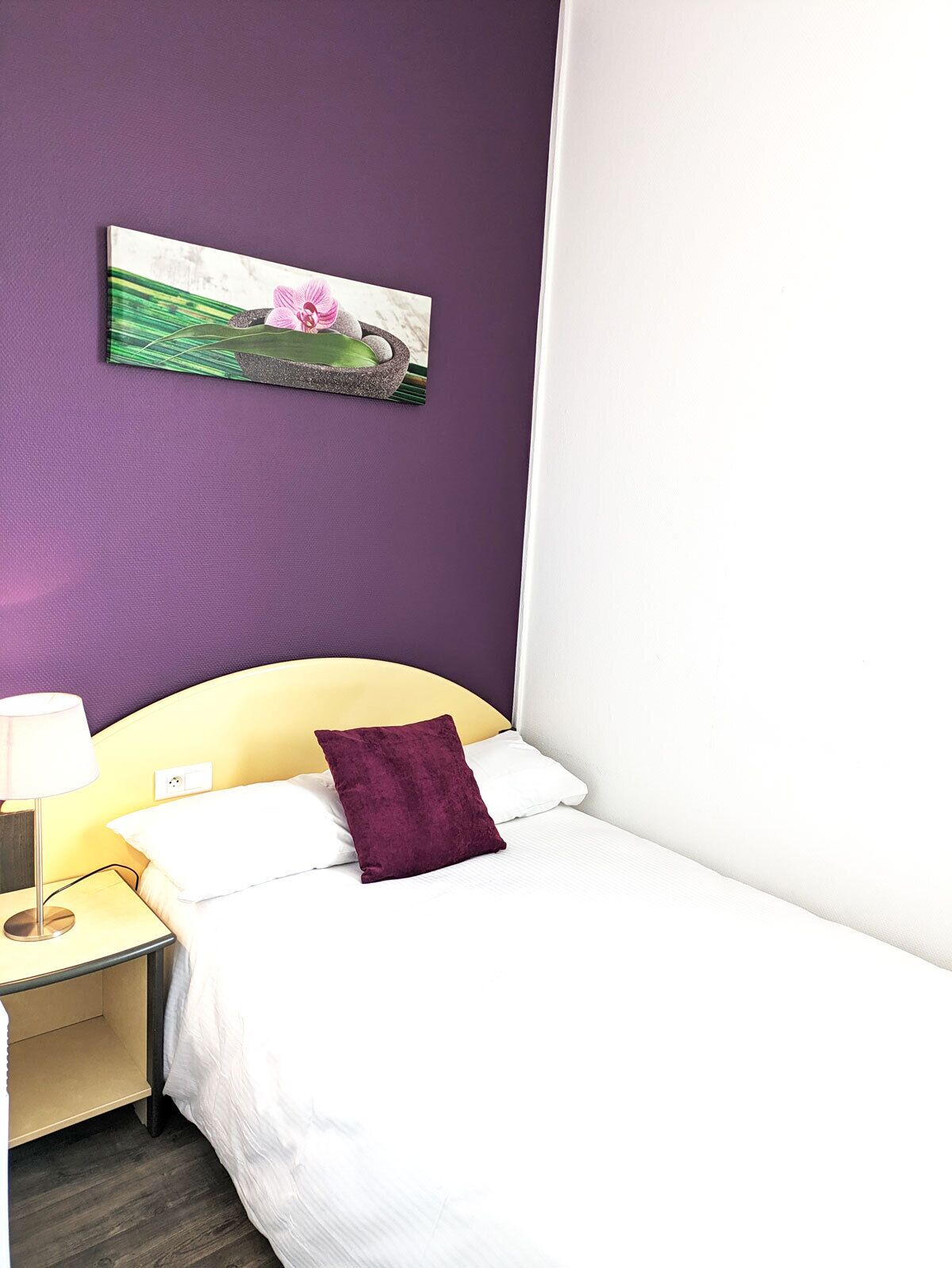 Una habitación de hotel con una cama, una mesita de noche, una lámpara y un cuadro en la pared.