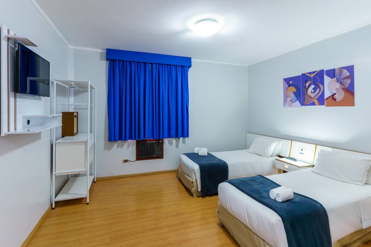 Une chambre d’hôtel avec deux lits, une télévision, une étagère et un tableau.