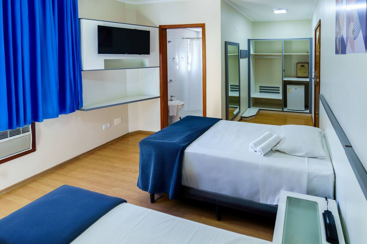 Une chambre d’hôtel avec deux lits, une télévision, une douche et une armoire.