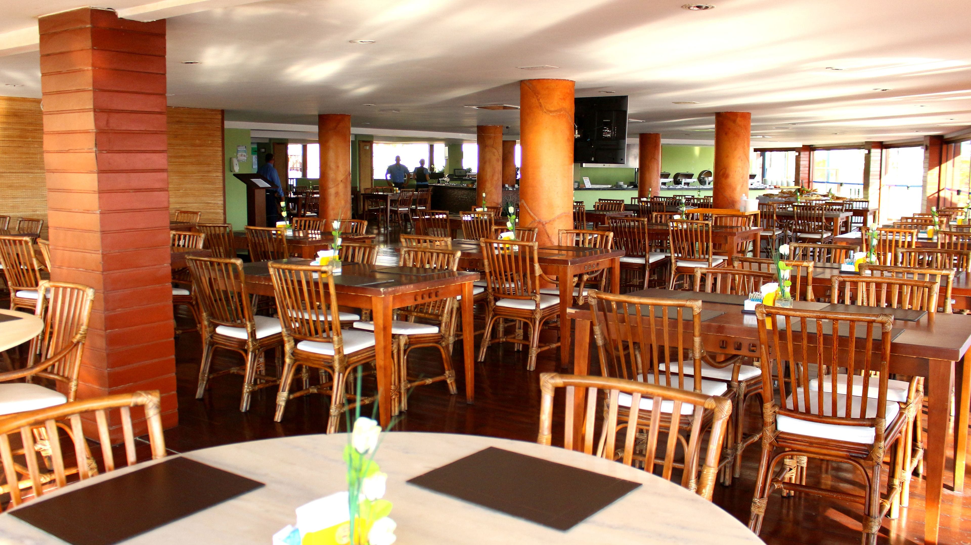 A spacious dining area with numerous wooden tables and chairs, large pillars, and a high ceiling.