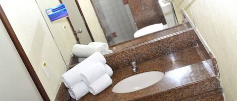 Un baño con encimera de granito, lavamanos y espejo. Hay toallas apiladas en la encimera.