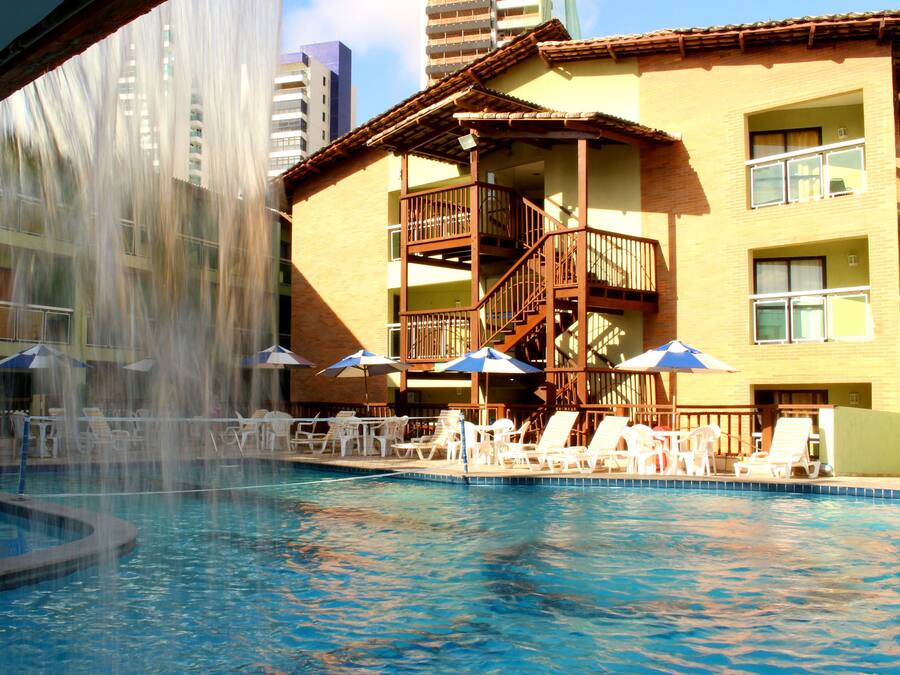 Zona de piscina d'hotel amb una font, seients de relax i ombrelles.