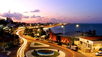 A coastal cityscape at dusk with a roundabout, a bridge, and a beach in the background.