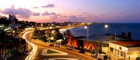 A coastal cityscape at dusk with a roundabout, a bridge, and a beach in the background.