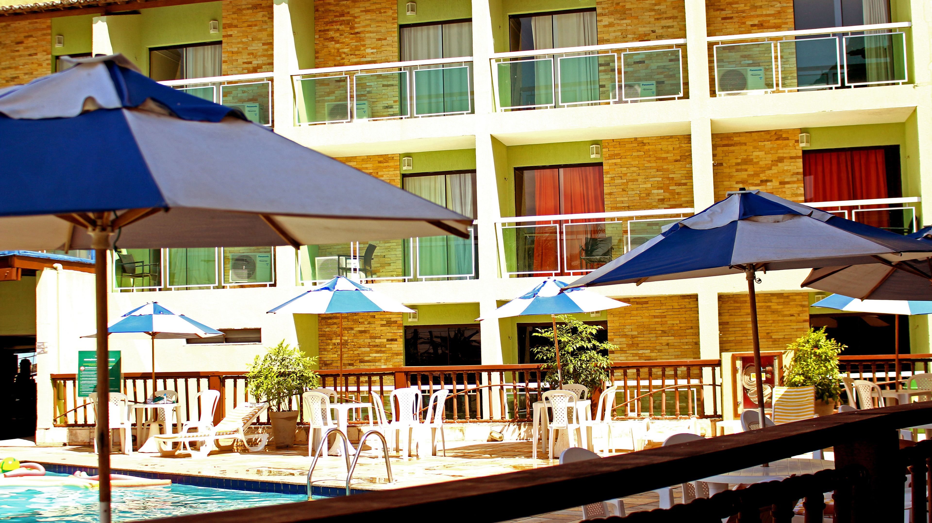 A pool area with multiple umbrellas, lounge chairs, and a building with balconies in the background.