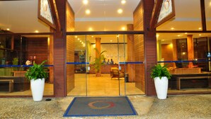 A hotel entrance with a reception desk, two potted plants, and a blue mat at the door. - Natal Praia Hotel (Natal)