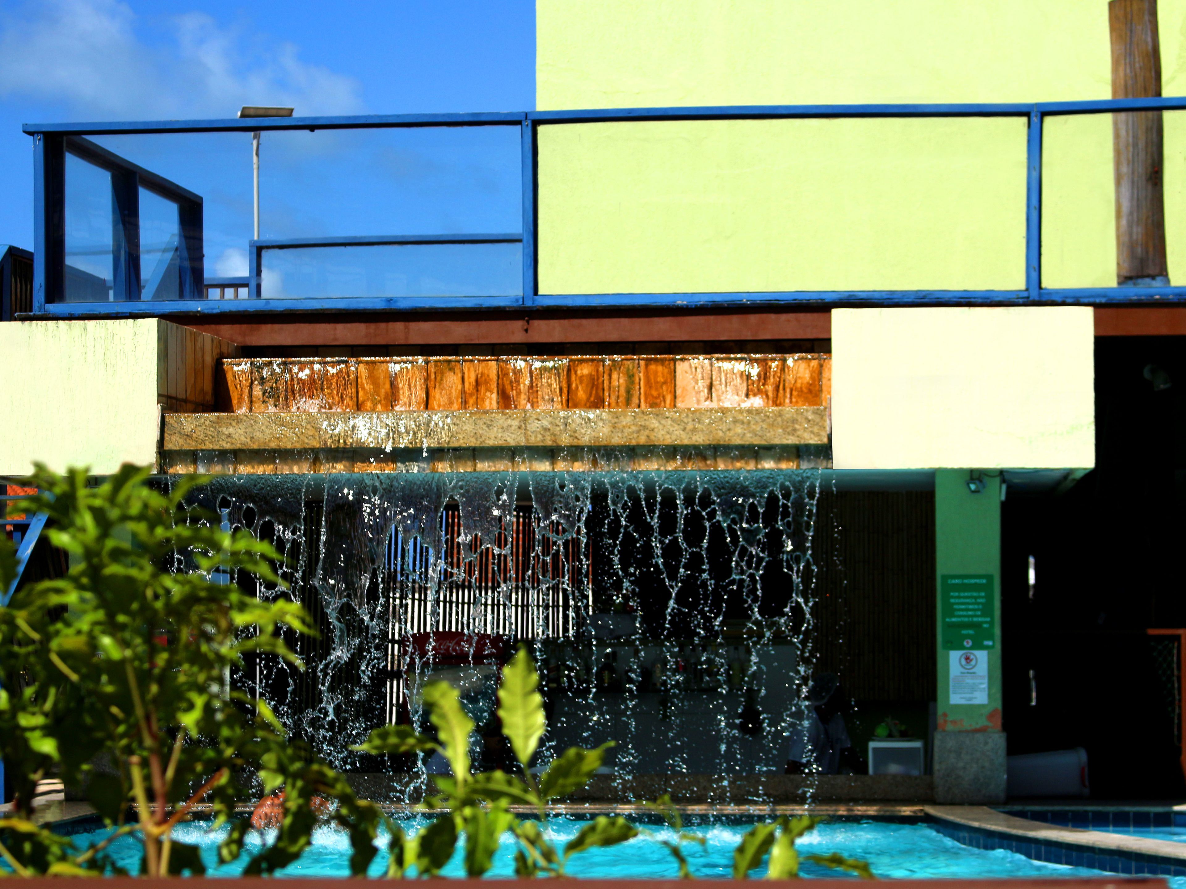 A pool with a waterfall feature, surrounded by greenery.