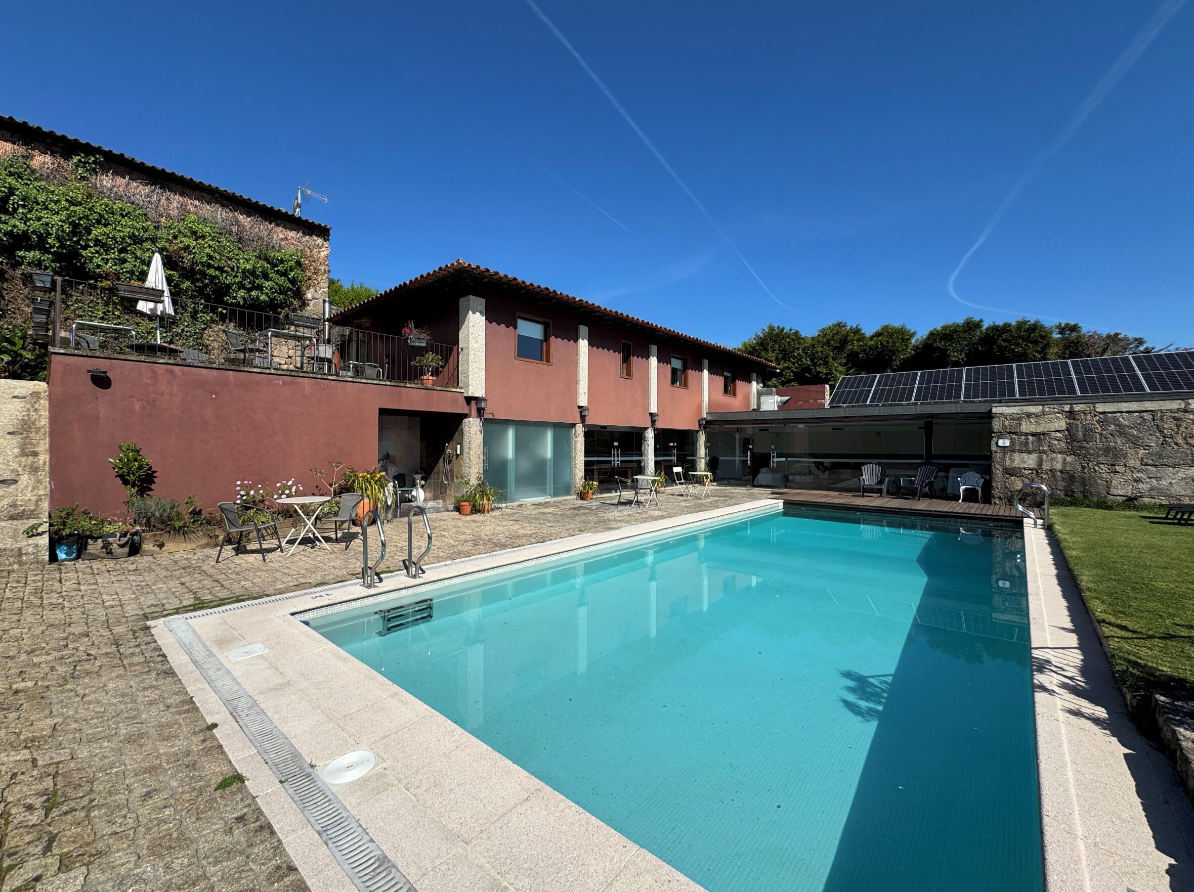 A swimming pool with a stone deck, a building with a red facade, and a solar panel array.