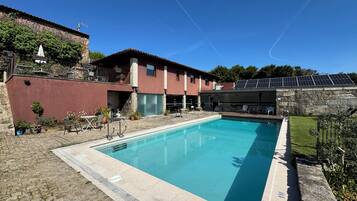 A swimming pool with a stone deck, a red building with a balcony, and solar panels on the roof.