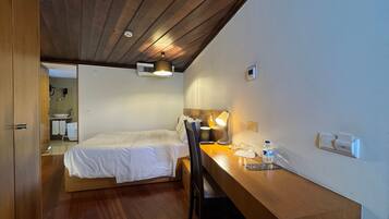 Una habitación con una cama, un escritorio con una lámpara y un espejo. Tiene techo de madera y aire acondicionado instalado en la pared.