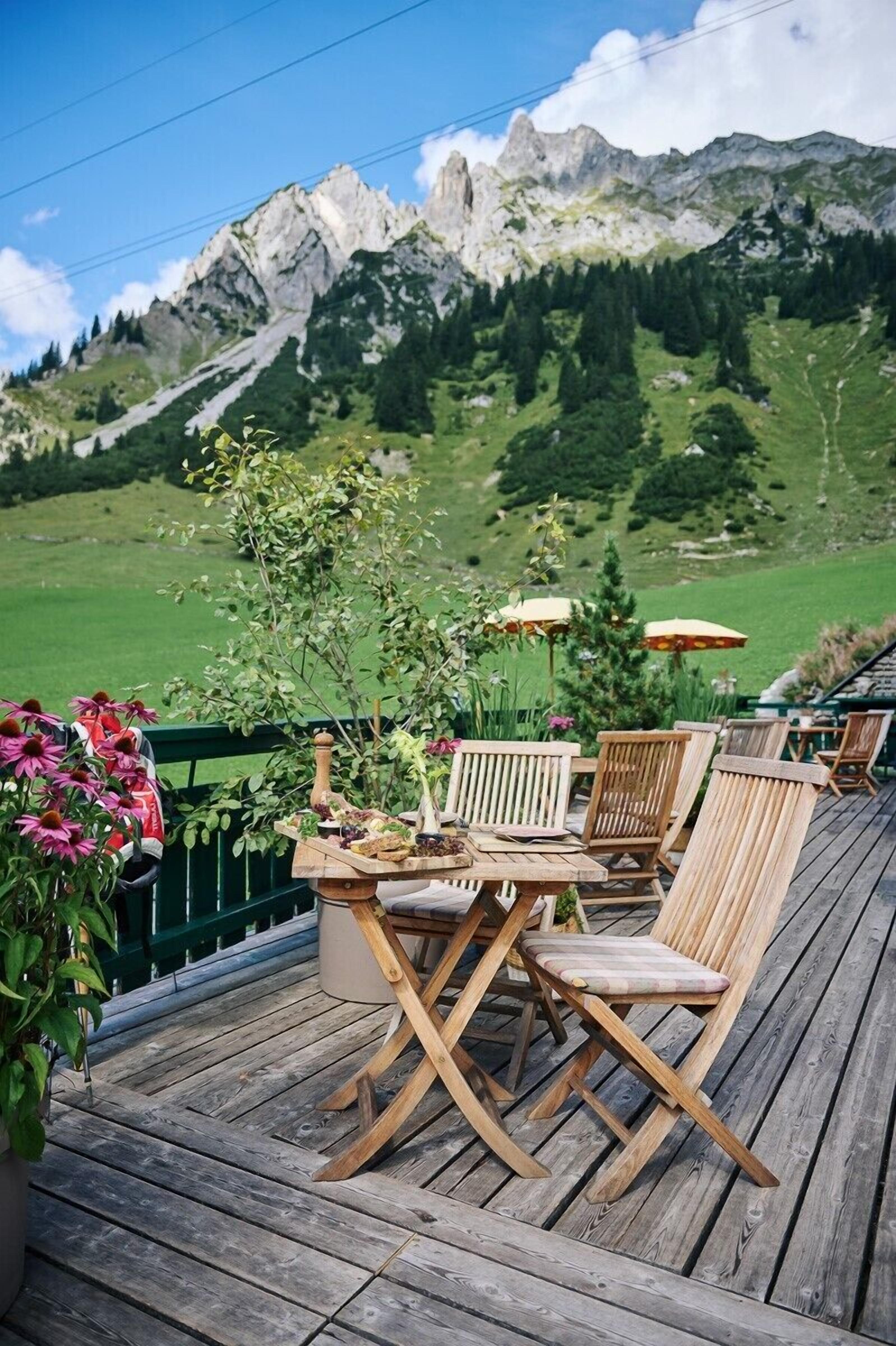 A wooden deck with outdoor furniture, a table with a centerpiece, and a view of mountains in the background.