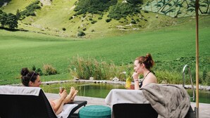 Dos sillones de relax en una terraza de madera con vistas a un lago y montañas al fondo.