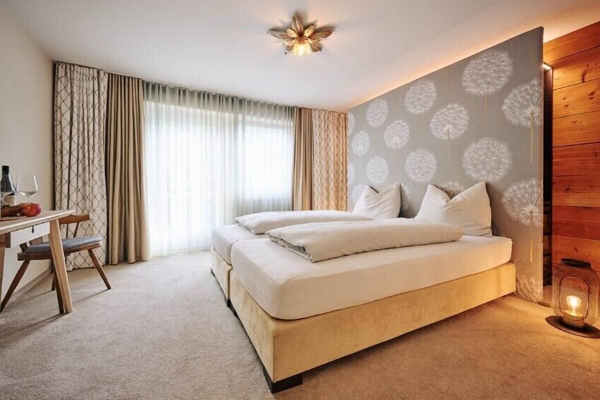 Een slaapkamer met een bed, een bureau met stoel, een lamp en een raam met gordijnen.